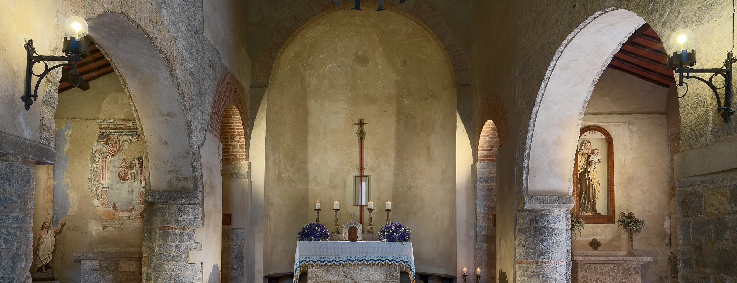 Inside the church: three naves under round arches, frescoes on the left wall, and the altar in the apse