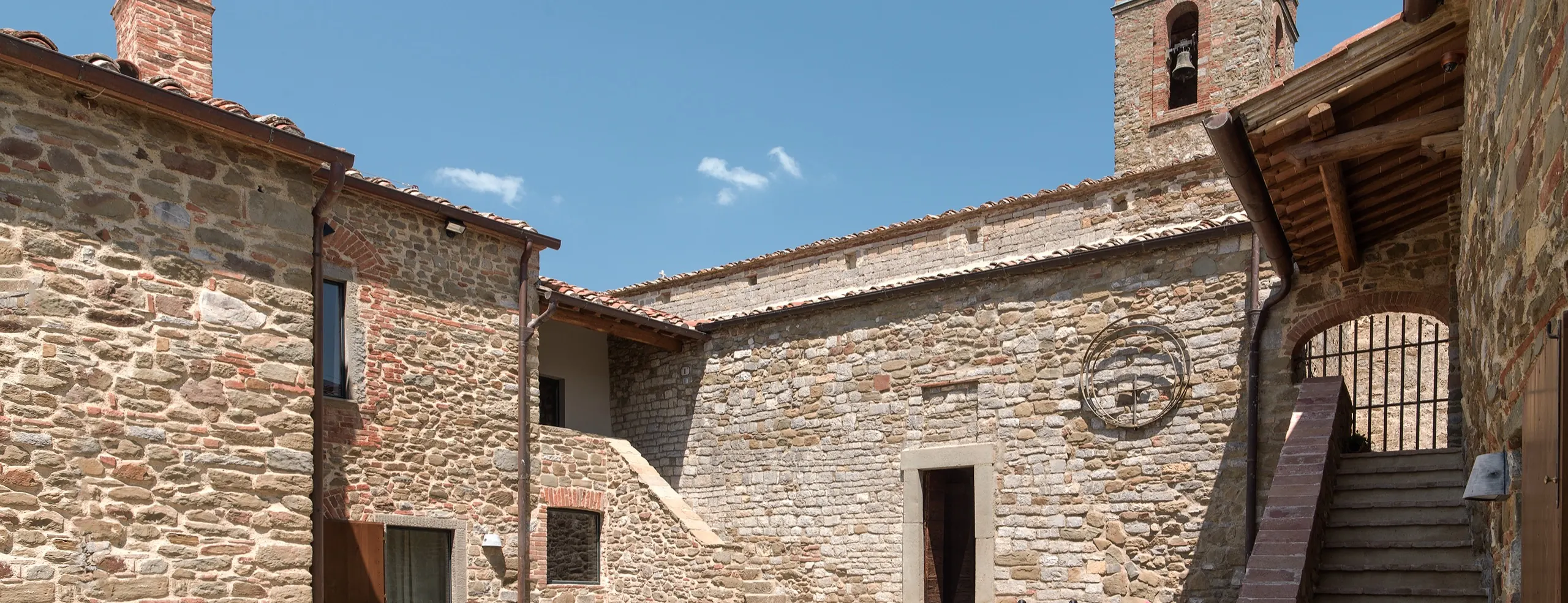 The paved courtyard of the house, stone walls and an outside stair, with the tower beyond