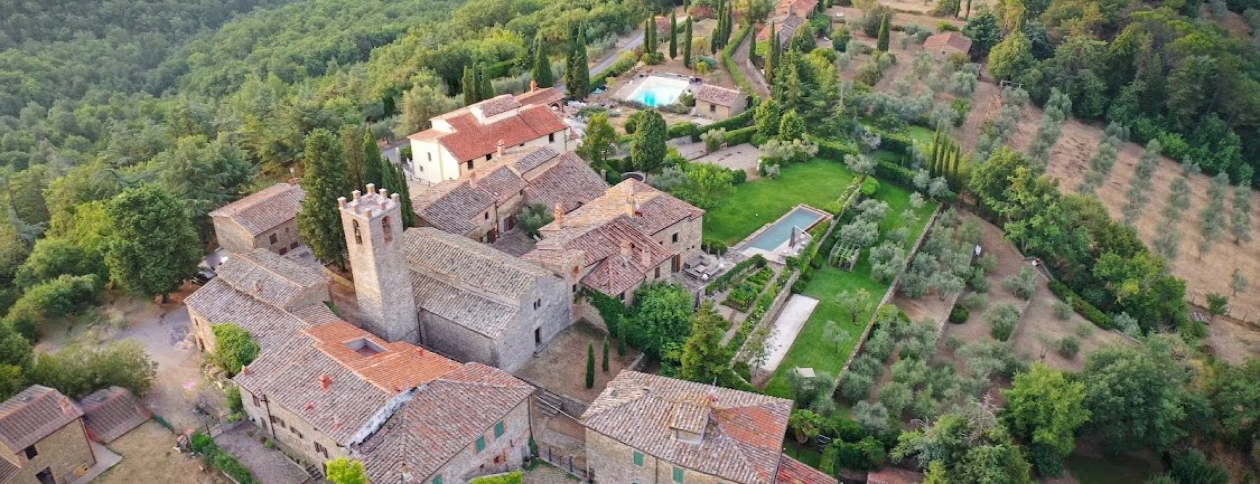 Il borgo di San Vincenti dall'alto: la chiesa e il suo campanile, le case in pietra, la piscina fra gli olivi e le colline boscose intorno